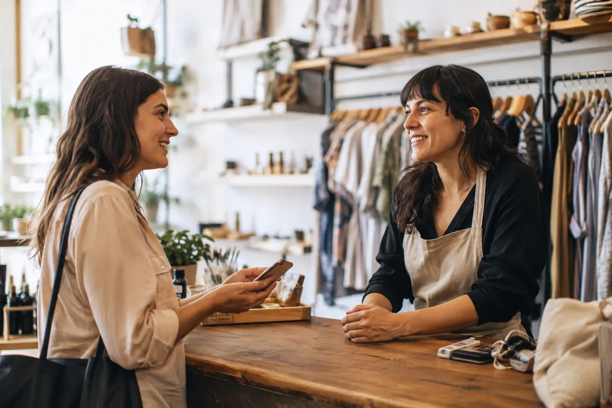 A freelancer and a small local business owner talking casually across a shop counter, both relaxed, natural light